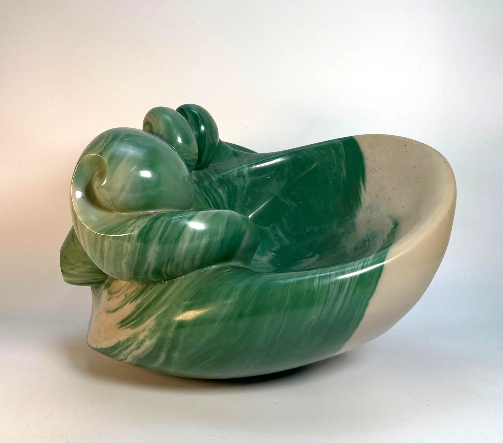 SCULPTURE GREEN MARBLE BY PEGGY MACH: A polished sculpture carved from green marble, with veins of white or lighter stone, depicts an abstract, flowing form. Dimensions: 12” h x 19” L x 12” W Artist or Maker: PEGGY MAC
