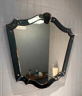 UNIQUE VENETIAN SMOKED GLASS WALL MIRROR: A Venetian wall mirror with a shield shape, featuring a dark blue glass frame with decorative scalloped edges and small circular accents. From the Moschino NYC showroom. Dimensions: 28.5” x 28.5