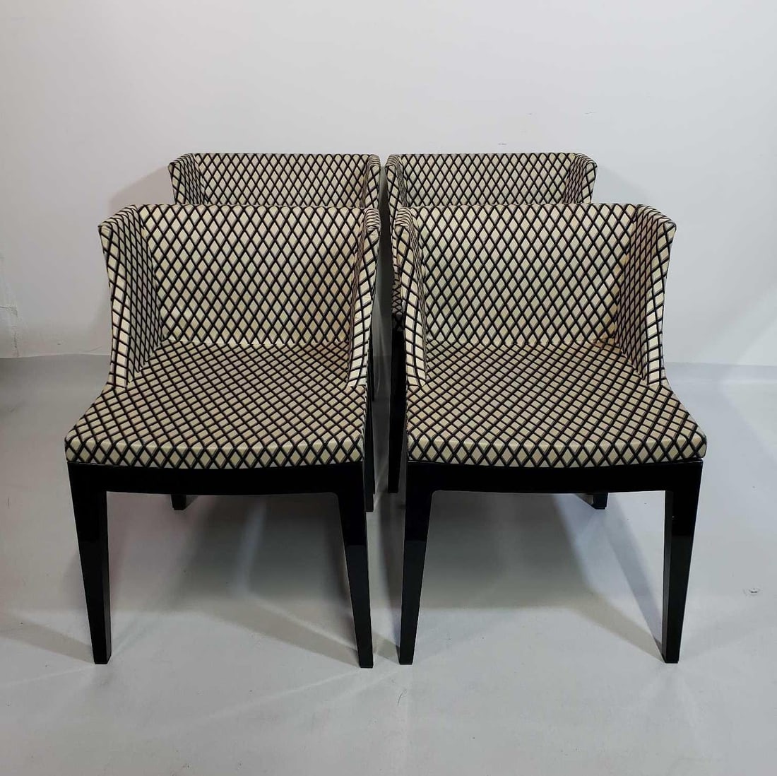 FOUR PHILIPPE STARCK FOR KARTELL MADEMOISELLE CHAIRS: Set of four Mademoiselle chairs designed by Philippe Starck for Kartell are shown. These chairs feature a black frame and are upholstered in a fabric with a repeating diamond harelquin pattern in shad