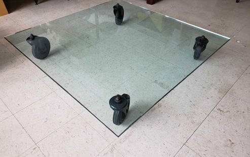 FONTANA ARTE TAVOLO CON RUOTE TABLE BY GAE AULENTI: A Fontana Arte "Tavolo con Ruote" coffee table designed by Gae Aulenti, featuring a thick rectangular glass top resting directly on four large, industrial-style spoked wheels. Dimensions: 10"h to top