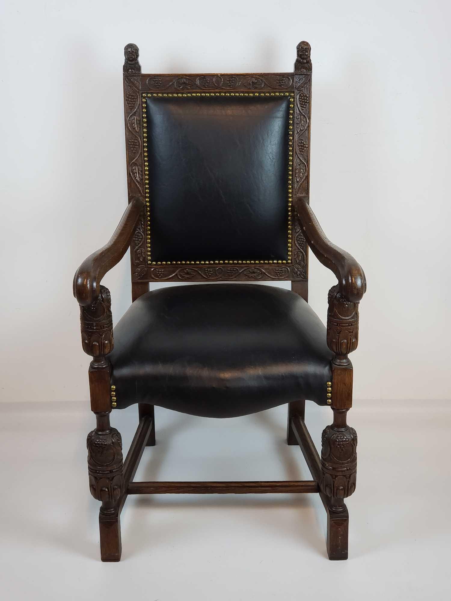 CARVED OAK BOBBIN TURNED THRONE CHAIR WITH GRAPE CLUSTER MOTIF: A carved oak bobbin turned throne chair, featuring a dark wood finish, an ornate grape cluster motif, and a studded black leather seat and back. Dimensions: 43"h x 23"w x 23"d Artist or
