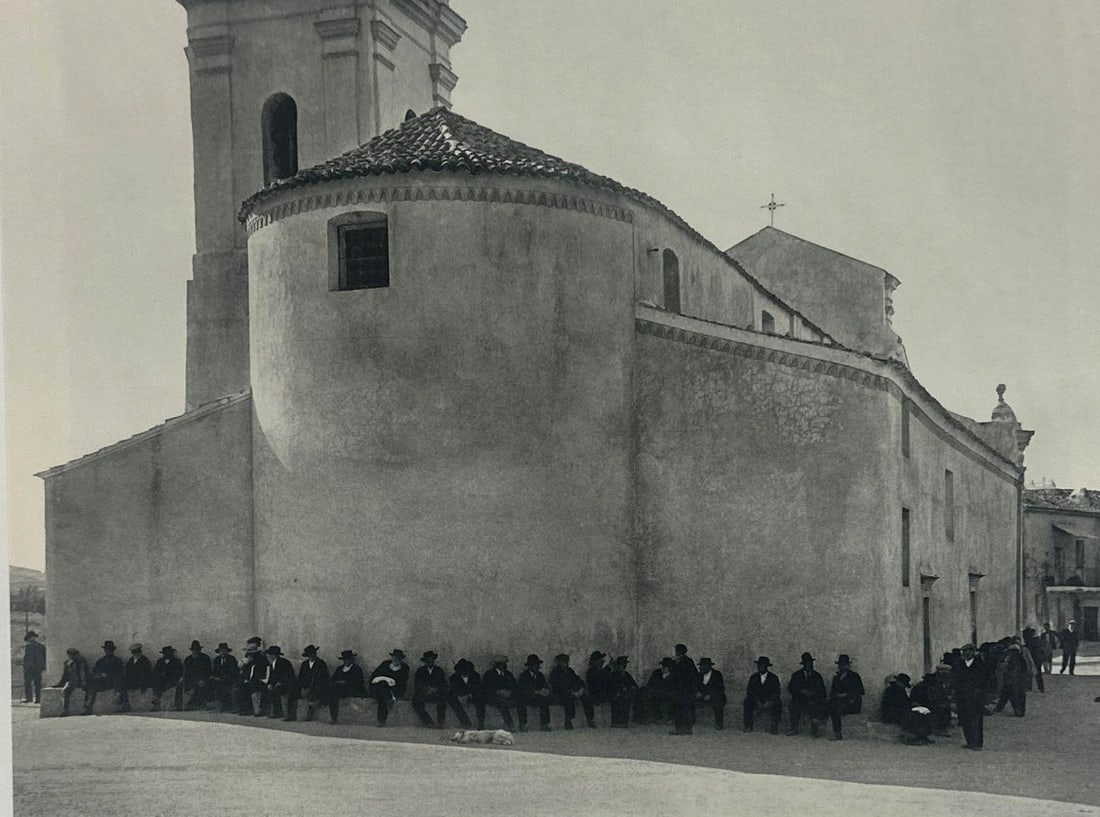 ANDRE KERTESZ, PIANA, 1932, CORSICA, SHEET-FED GRAVURE. 1972 FRANCE: A black and white image depicting a towering church and a line of men seated along its perimeter. (with certificate of authenticity) Dimensions oa: 16" x 12" image: 7.25" x 9.5" Arti