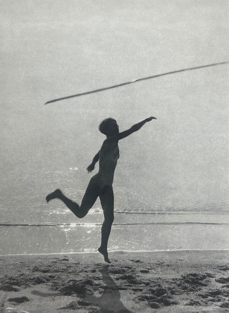 PIERRE BOUCHER, SAINT-TROPEZ, 1933, SHEET FED GRAVURE, 1985 PARIS, FRANCE: A black and white photo print depicting a silhouetted woman in the nude, captured mid-stride on a beach with a visible horizon line, throwing a javelin-like spear. (with certificate of authenticity) D