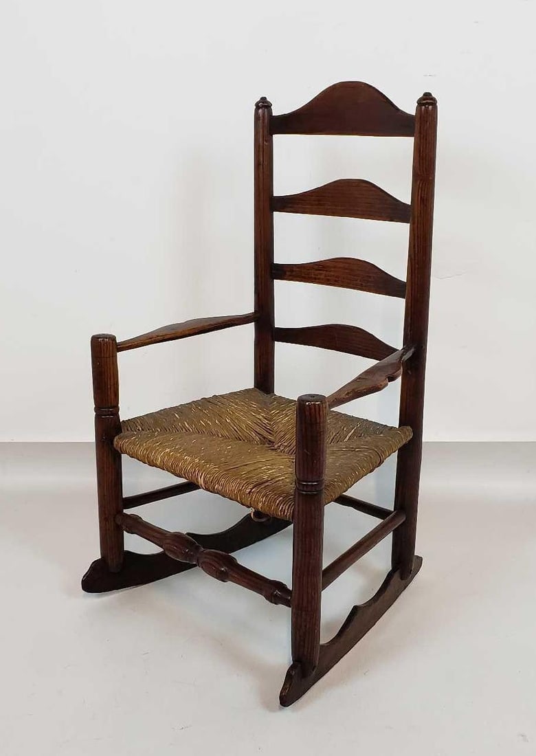 VALUE LOT ANTIQUE RUSH SEAT CHILD'S ROCKING CHAIR: A antique rush seat child's rocking chair. The chair is constructed from dark wood, featuring a tall ladder-back design and a woven rush seat. Dimensions: 29.5"h x 17.5"w x 17"d Arti