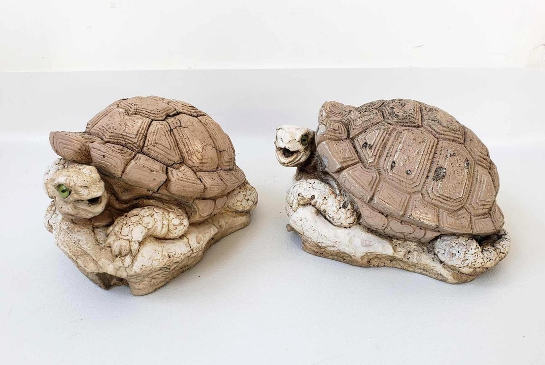 PAIR OF VINTAGE CEMENT TORTOISE FOUNTAINS: A pair of resting tortoise garden sculptures made from light-colored cement. Both have green eye detail. Dimensions: 6”T x 11” x 9” Artist or Maker: Signed, indecipherable. Dated 1