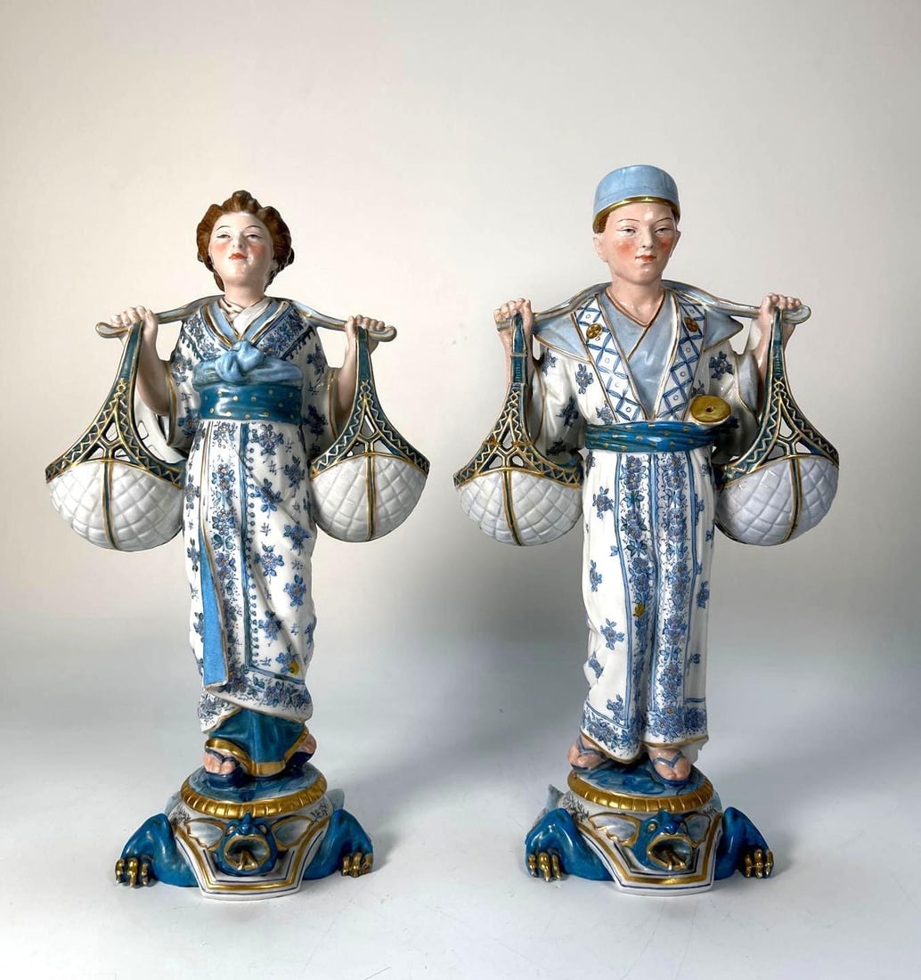 PAIR OF VINTAGE DERBY / CROWN DERBY STYLE PORCELAIN FIGURES | CHINOISERIE WATER CARRIERS: *A pair of vintage Derby / Crown Derby style porcelain figures, depicting a male and female figure carrying baskets, adorned with intricate blue and white floral patterns and rich gilding on their rob
