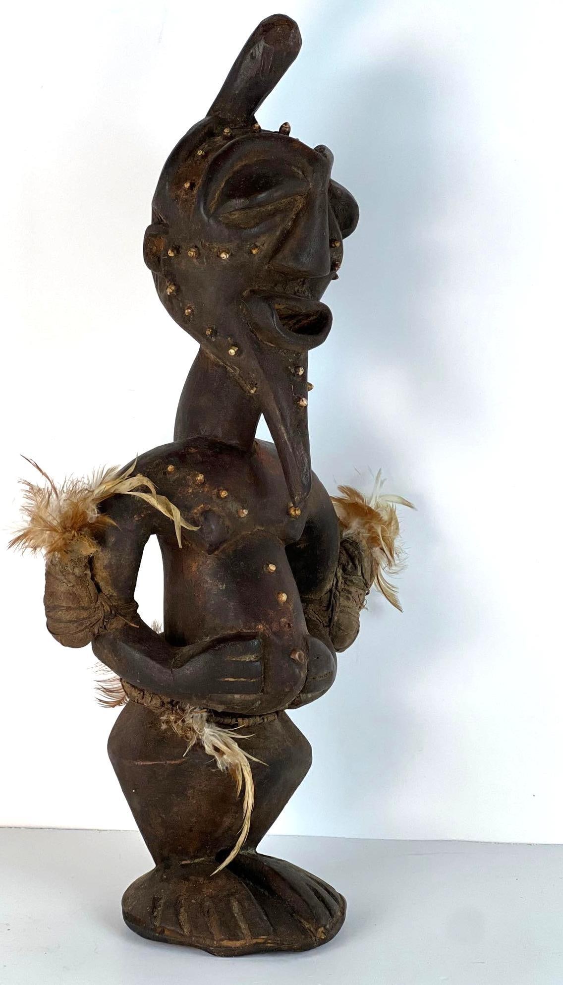 ANTIQUE WOODEN MALE STATUE W/ FEATHERS IN SONGYE STYLE: *African Carved Wooden Male Figure decorated with shells and feathers. From the estate of a New York private collector of African and Asian art. Dimensions: 19.5" T X 8.5" W Artist or Maker: Unknown N