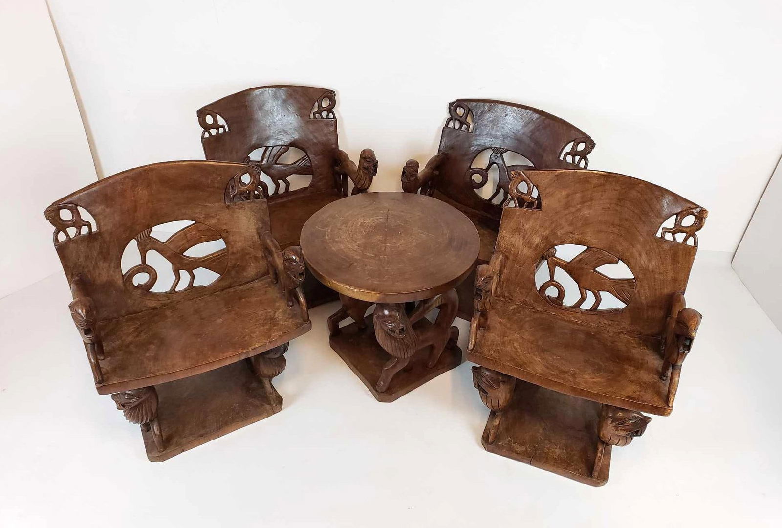 VINTAGE AFRICAN CARVED TIGRESS WOOD ANIMAL FIGURAL TABLE AND FOUR CHAIRS: *A dark wood dining set consisting of a round table and four chairs, all hand carved with animal figures and cut-out designs. All four chairs vary slightly in size due to their handmade nature. Likely