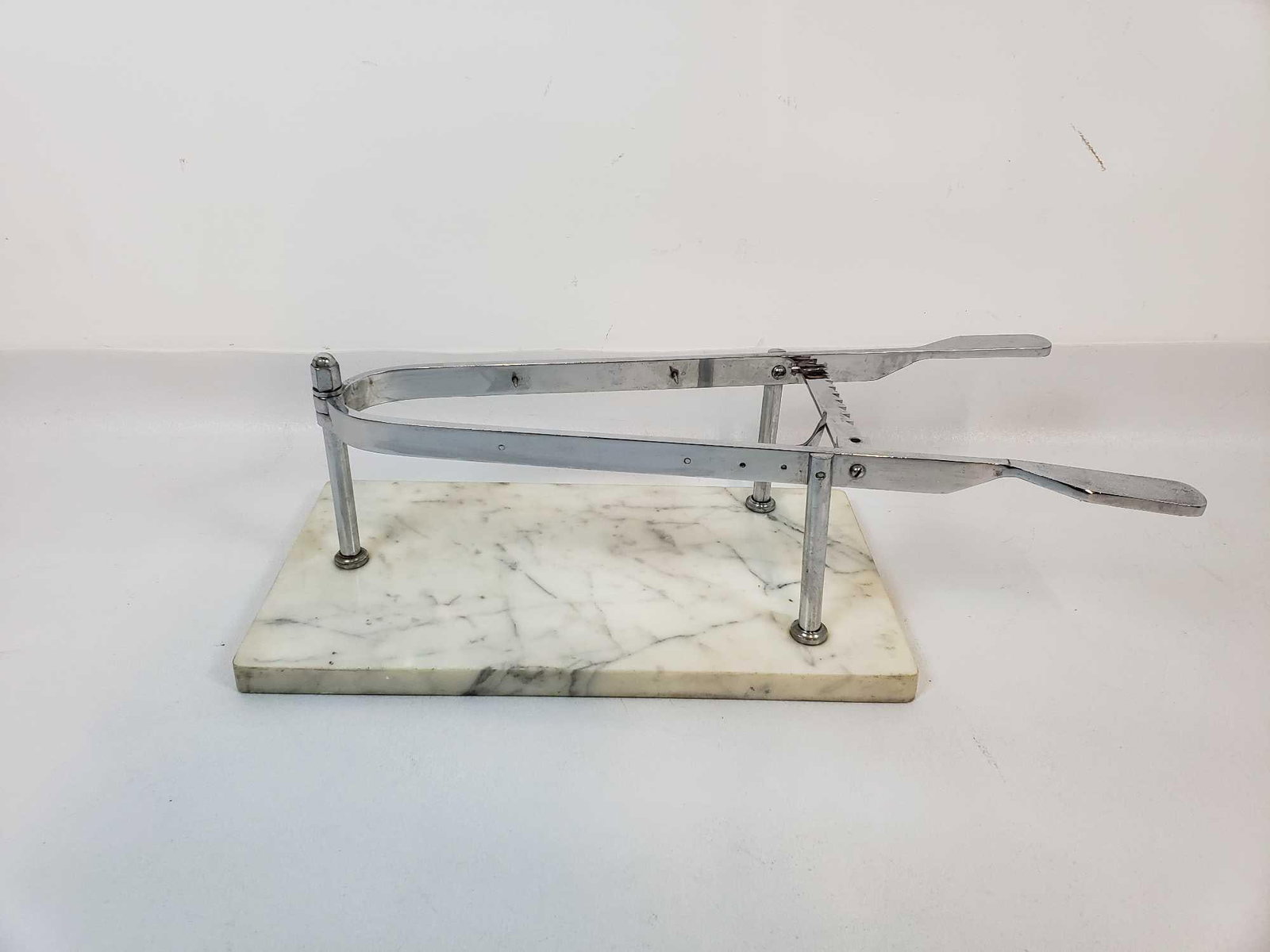 VINTAGE STAINLESS STEEL AND MARBLE PORTE JAMBON HAM HOLDER: *A vintage stainless steel and marble "porte jambon" ham holder. It features a polished stainless steel frame, designed to hold a ham in place for carving, mounted on a rectangular white marble base. 