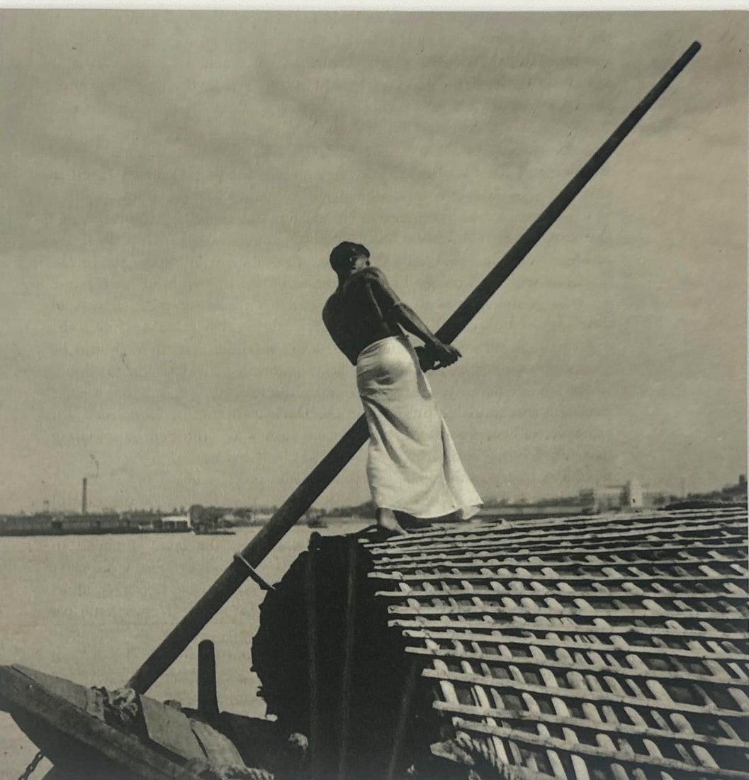 EUSTON SEALY, THE HELMSMAN, SHEET FED GRAVURE, 1940 GREAT BRITAIN: *A black and white photo print depicting a shirtless figure piloting a boat. (with certificate of authenticity) Dimensions oa: 16" x 12" image: 7" x 7" Artist or Maker: Euston Sealy Pr