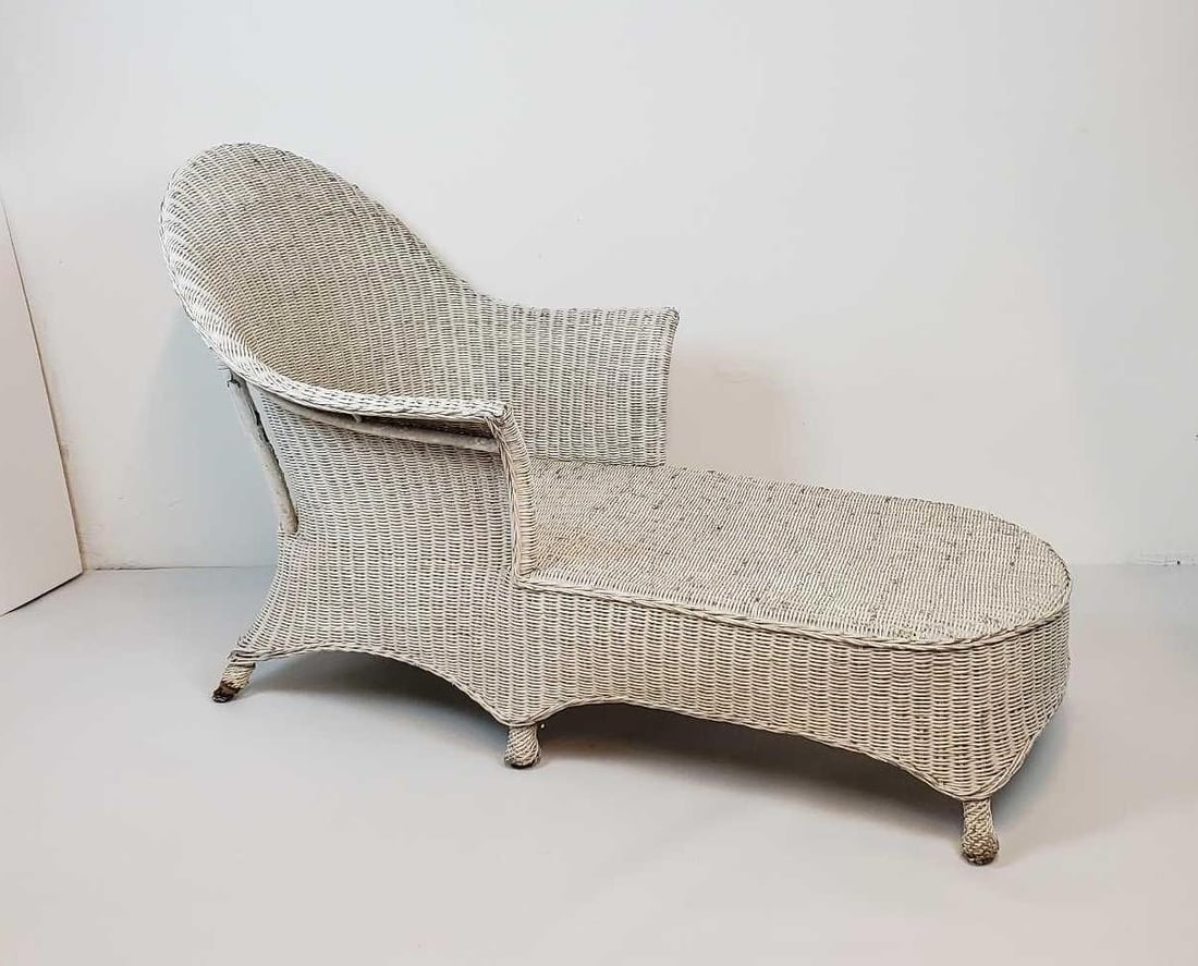 ANTIQUE WICKER RECAMIER / DAYBED: An antique wicker recamier crafted from woven wicker, this chaise lounge features a gracefully curved back and armrest on one side, flowing into an elongated seat. Dimensions: Artist or Maker: Unkno