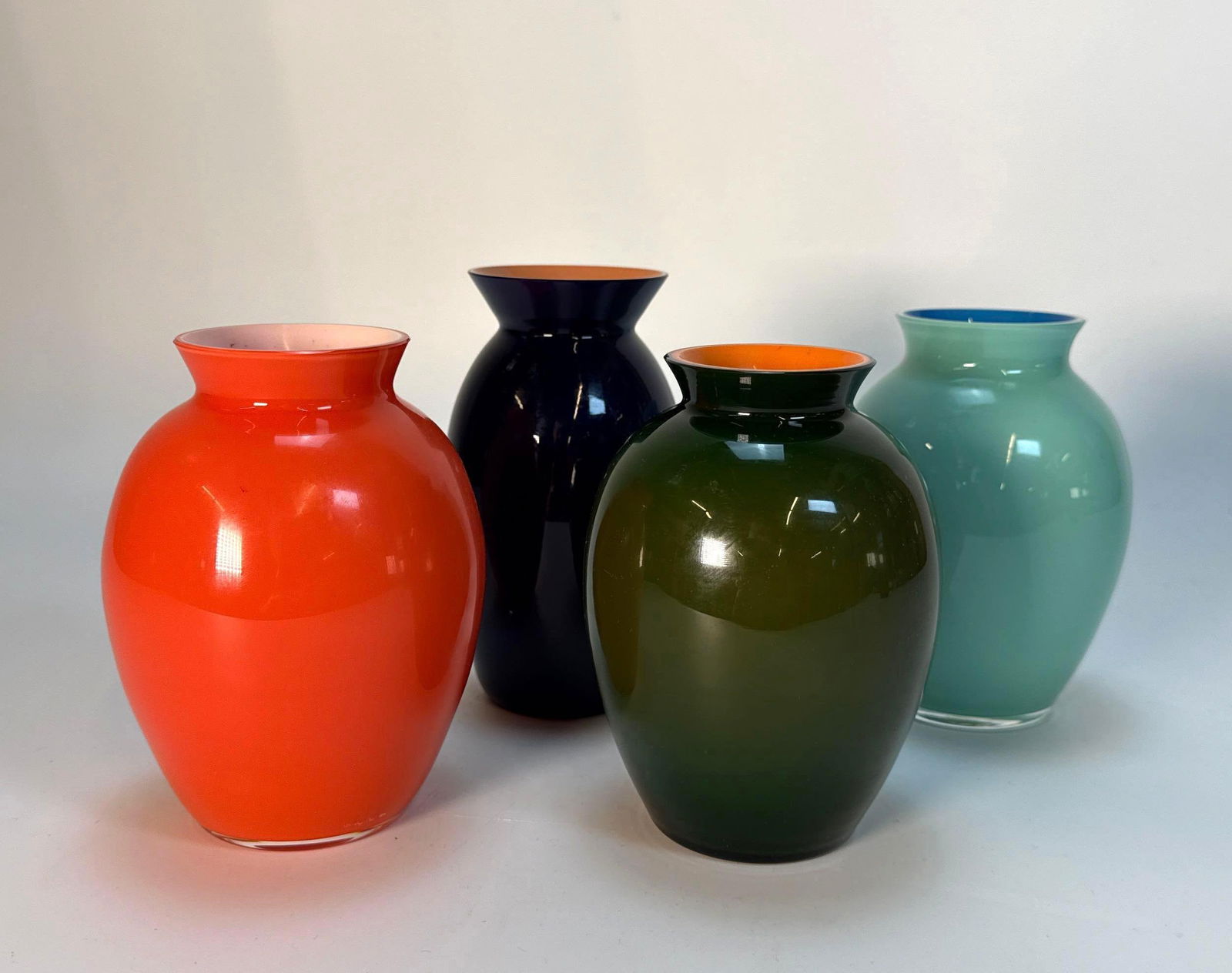 FOUR CARLO MORETTI SIGNED MURANO VASES: Four petite uniform shaped vases / vessels in vibrant, glossy colors: orange, dark green, turquoise, and navy blue. Tallest Dimensions: 5” Artist or Maker: Carlo Moretti Provenance: From a Ne
