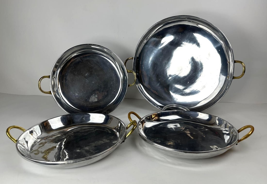 QUARTET OF HECHO A MANO SOUTHAMPTON ALUMINUM PLATTERS: A hand-made quartet of aluminum serving platters, comprised of four round pieces of two sizes, all featuring brass handles. Dimensions: 13.5"DIA & 18"DIA Artist or Maker: Cynthia Rapprt Ba