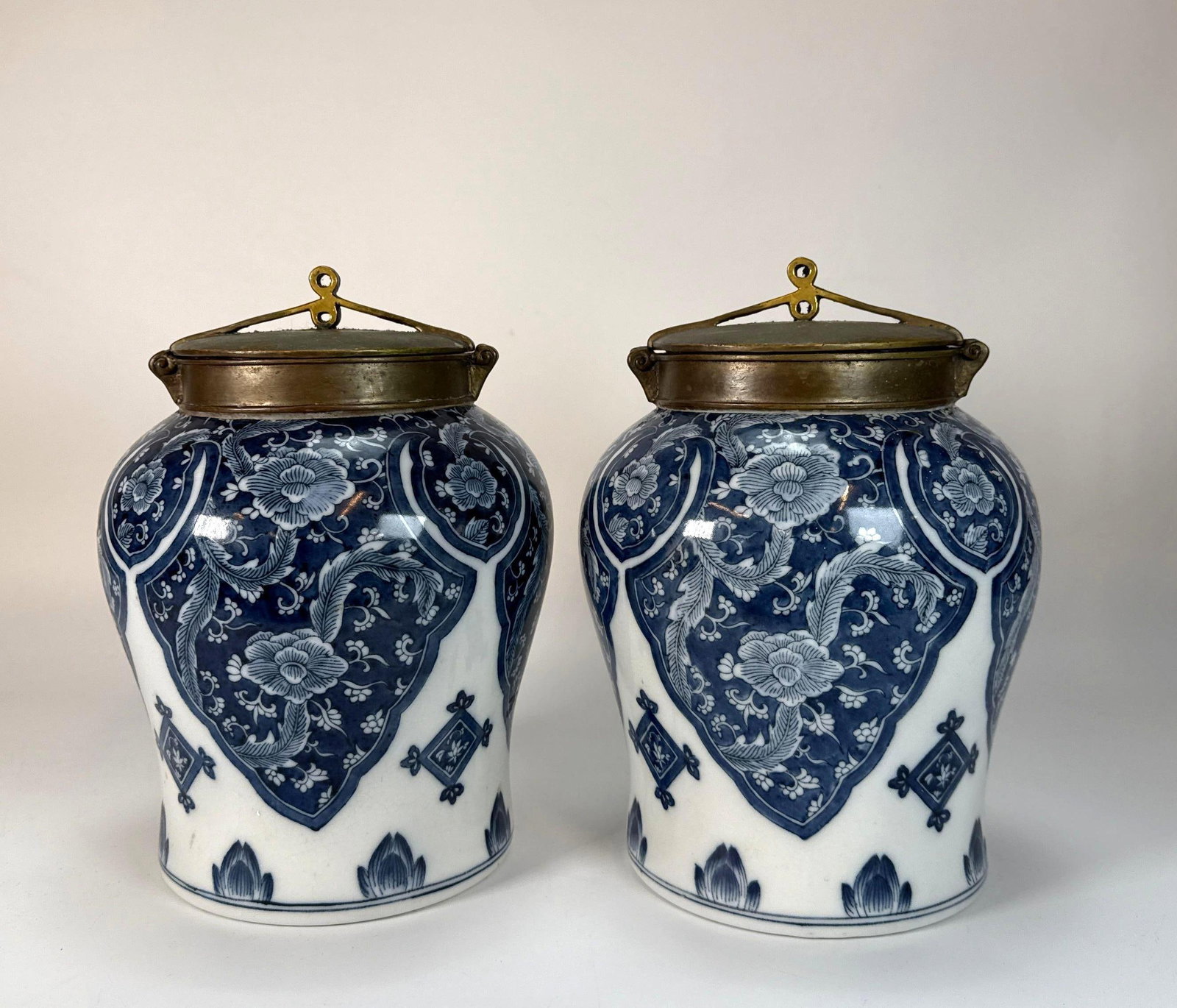 PAIR OF CHINESE GINGER JARS: A pair of blue and white porcelain ginger jars with ovoid bodies, decorated with underglaze cobalt floral and leaf motifs in reserved panels, and topped with domed brass lids featuring a finial loop. 