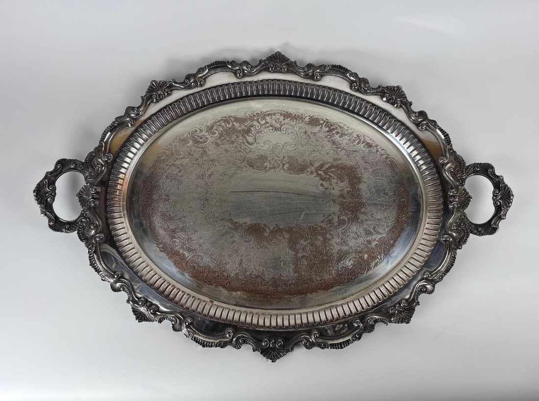 CHIPPENDALE BY WALLACE SILVER-PLATED SERVING TRAY: *A large, oval silver-plated serving tray with two ornate handles and a scalloped, raised edge, featuring an engraved center with floral and scroll motifs. X151 "Chippendale" style by Wallace. Dimens