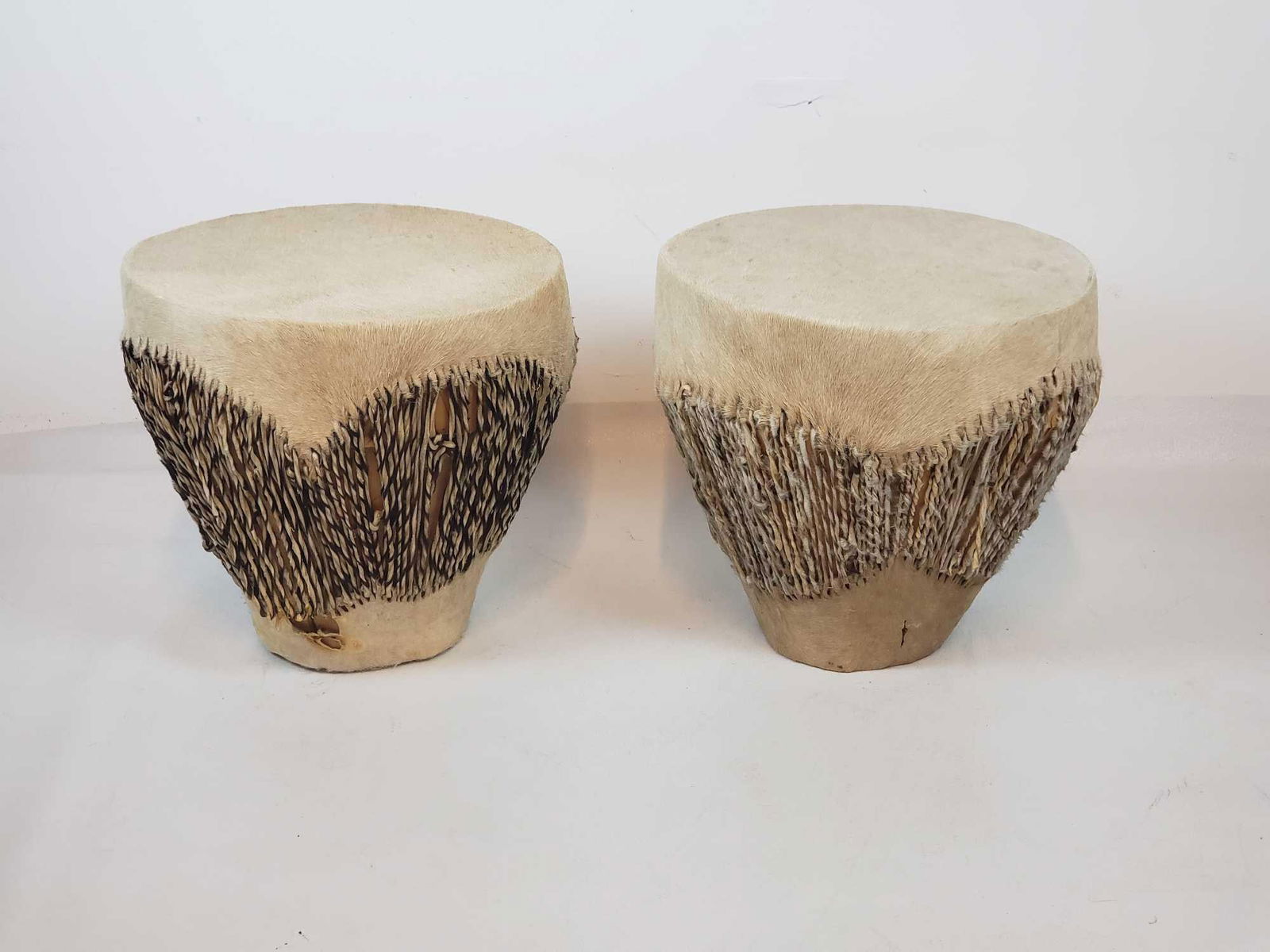 PAIR OF HIDE COVERED WOOD EMBUUTO / DJEMBE DRUMS: Pair of African Tribal Drums with Hair-on-Hide and Rope Lacing Dimensions: 14.5"h x 15.5"dia Maker: Unknown Provenance: A New York Collector Notes: Although care is taken to photograph a