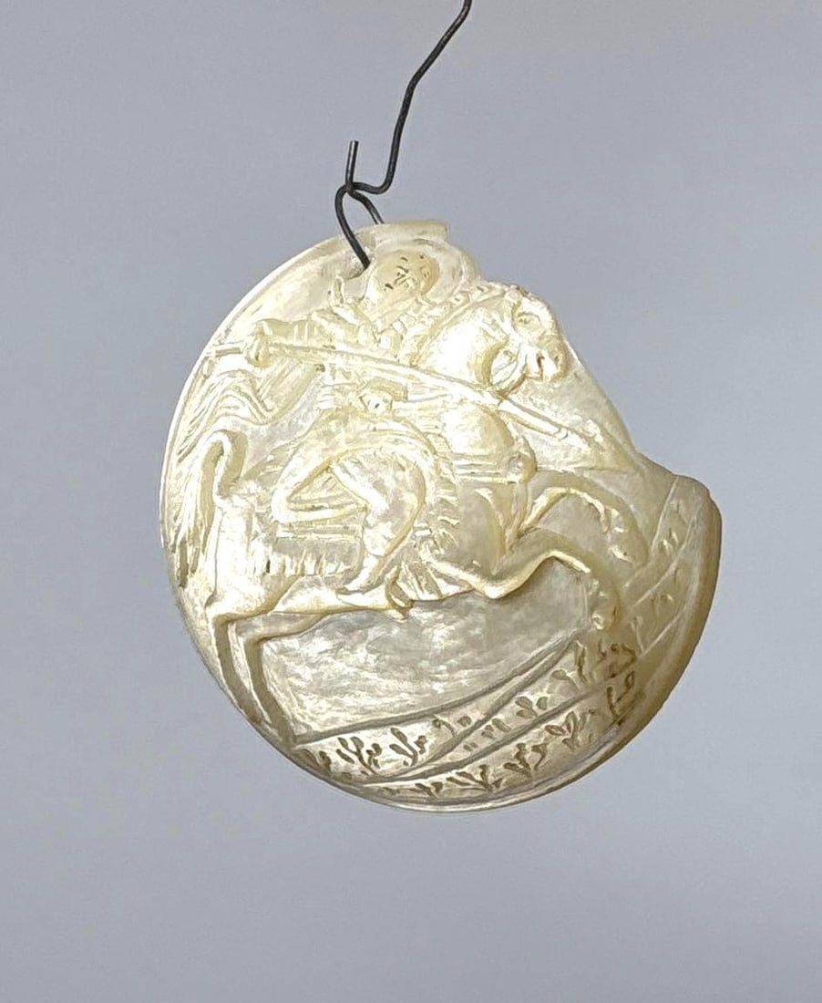 ANTIQUE ENGRAVED MOTHER OF PEARL SHELL CAMEO SAINT GEORGE AND THE DRAGON: A piece of engraved mother-of-pearl is a cameo carving depicting Saint George and the Dragon. Dimensions: 2" dia Maker: Unknown Provenance: A New York Collector Notes: Although care is tak