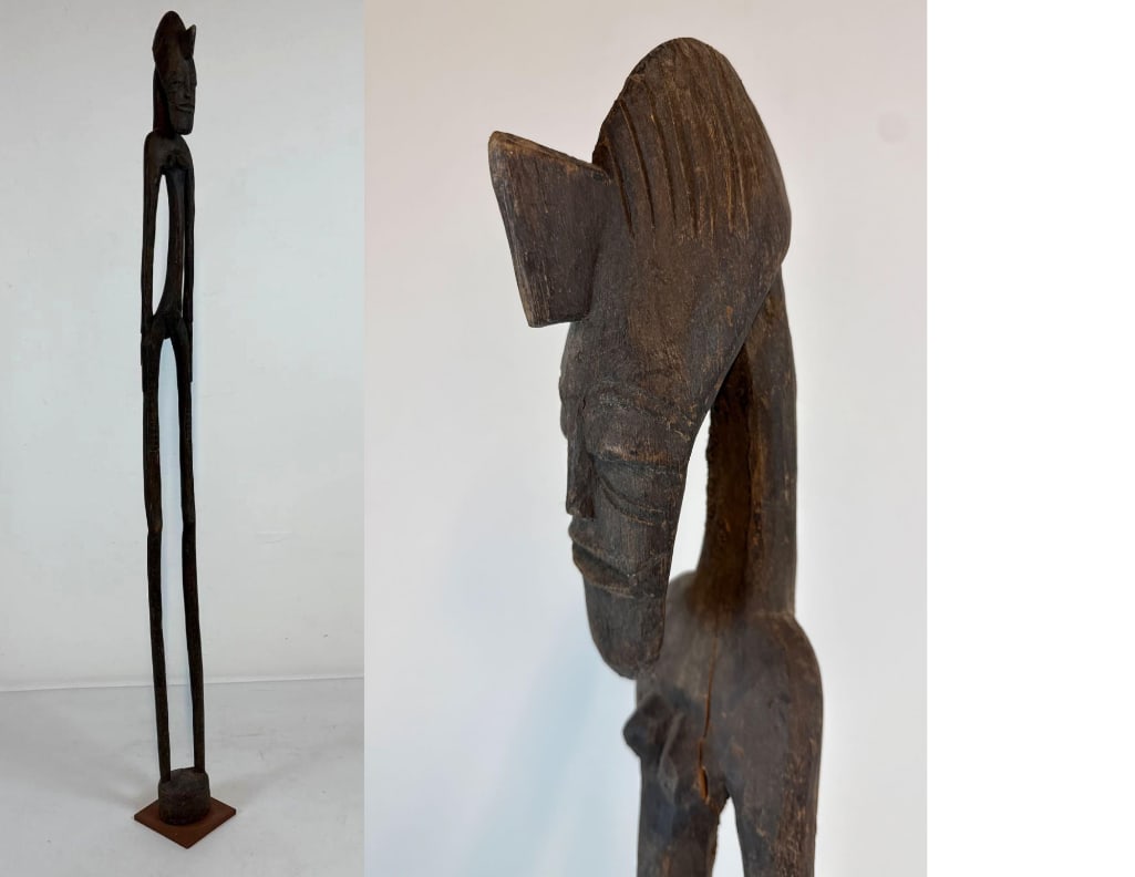 AFRICAN RHYTHM POUNDER FIGURE - IMPRESSIVE LONG WOOD CARVING: A longwood scuture on a metal base. Dimensions: 62" tall Maker: Unknown Provenance: A New York Collector Notes: Although care is taken to photograph and describe the item,