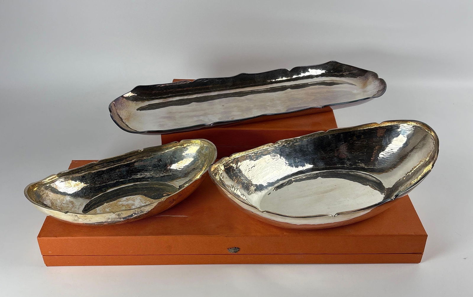 TRIO SANDRA JORDAN HAMMERED SILVER PLATE SERVEWARE LOT | MODERN HOLLOWARE BOWLS & LONG RECT.: This lot includes a trio of Sandra Jordan hammered silver-plated holloware, including a long rectangle tray, a bread bowl, and a shallow dish, all of a striking, organic, contemporar