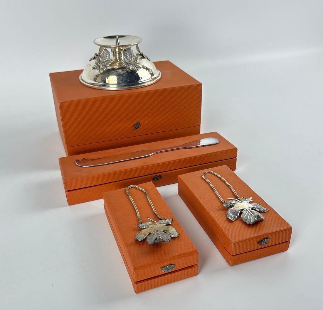 SANDRA JORDAN SILVER PLATED GIFT LOT (4 ITEMS) CANDLE HOLDER WINE LABLES CHEESE KNIFE CASED: This lot is a four-piece, cased, silver-plated gift set by Sandra Jordan, featuring a maple leaf design on a candle holder, two wine bottle labels, and a cheese knife, all presented in original boxes.