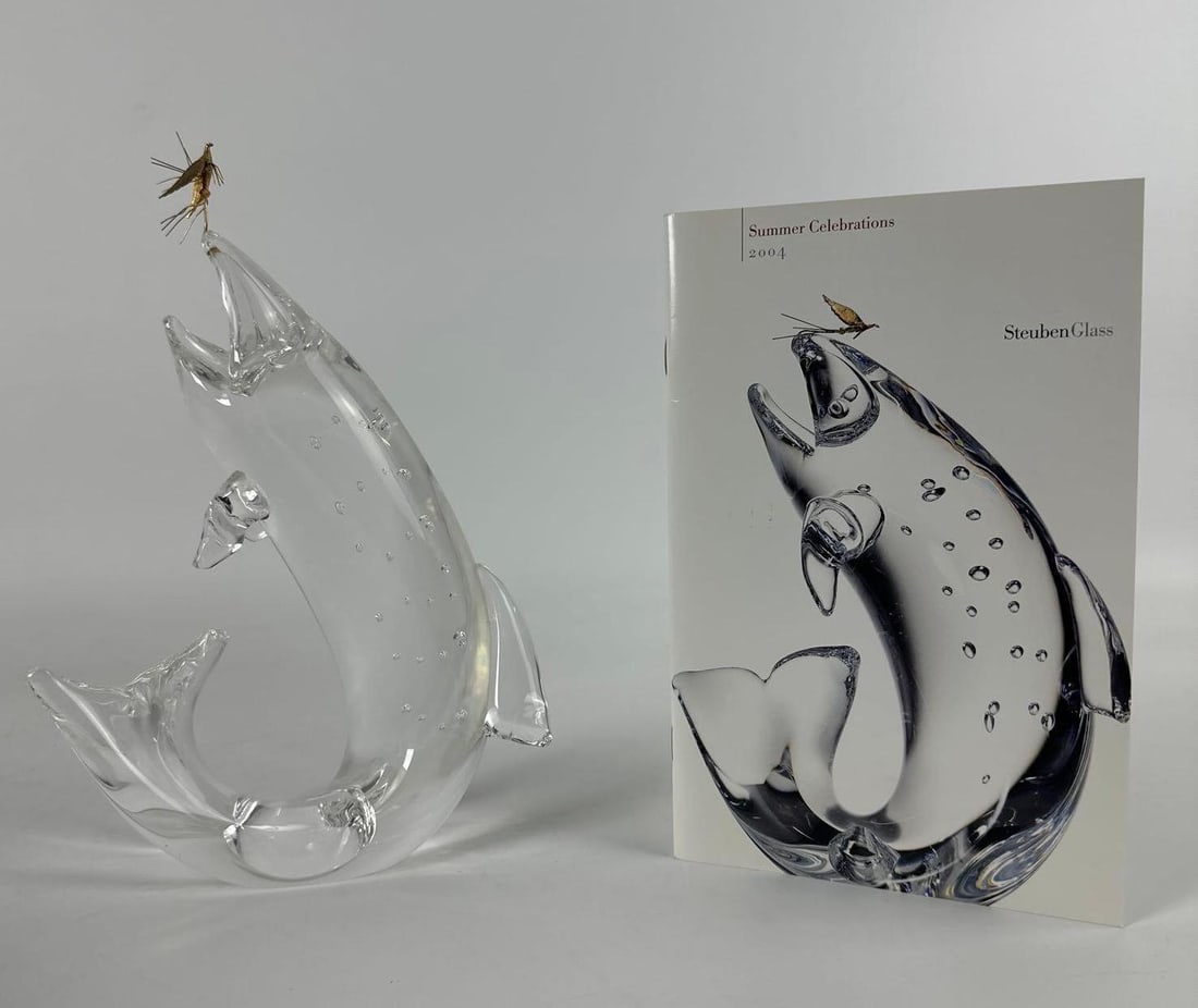 STEUBEN CRYSTAL "TROUT AND FLY" SCULPTURE BY JAMES HOUSTON WITH 18K GOLD FLY (C. 1966): This iconic sculpture designed by James Houston depicts a leaping trout with internal air bubble decoration, mouth open to catch an actual 18k gold fly lure. Dimensions: 10”H x 7”W x 3&rdq