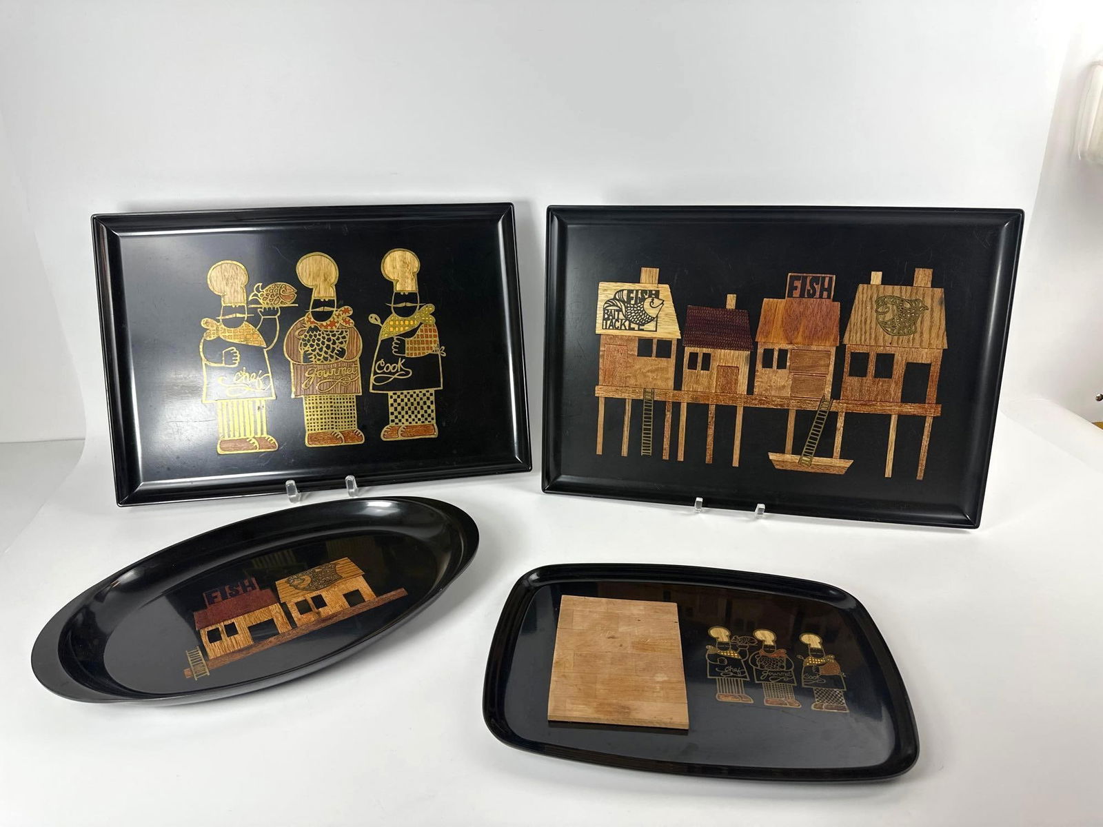 FOUR COUROC CALIFORNIA MID CENTURY MODERN TRAYS: A group of four black trays with inlaid wood veneer depicting different scenes. Largest Dimensions: 12.5"L x 18"W Maker: Couroc Provenance: The Estate of Joseph Rodano Notes: Althou