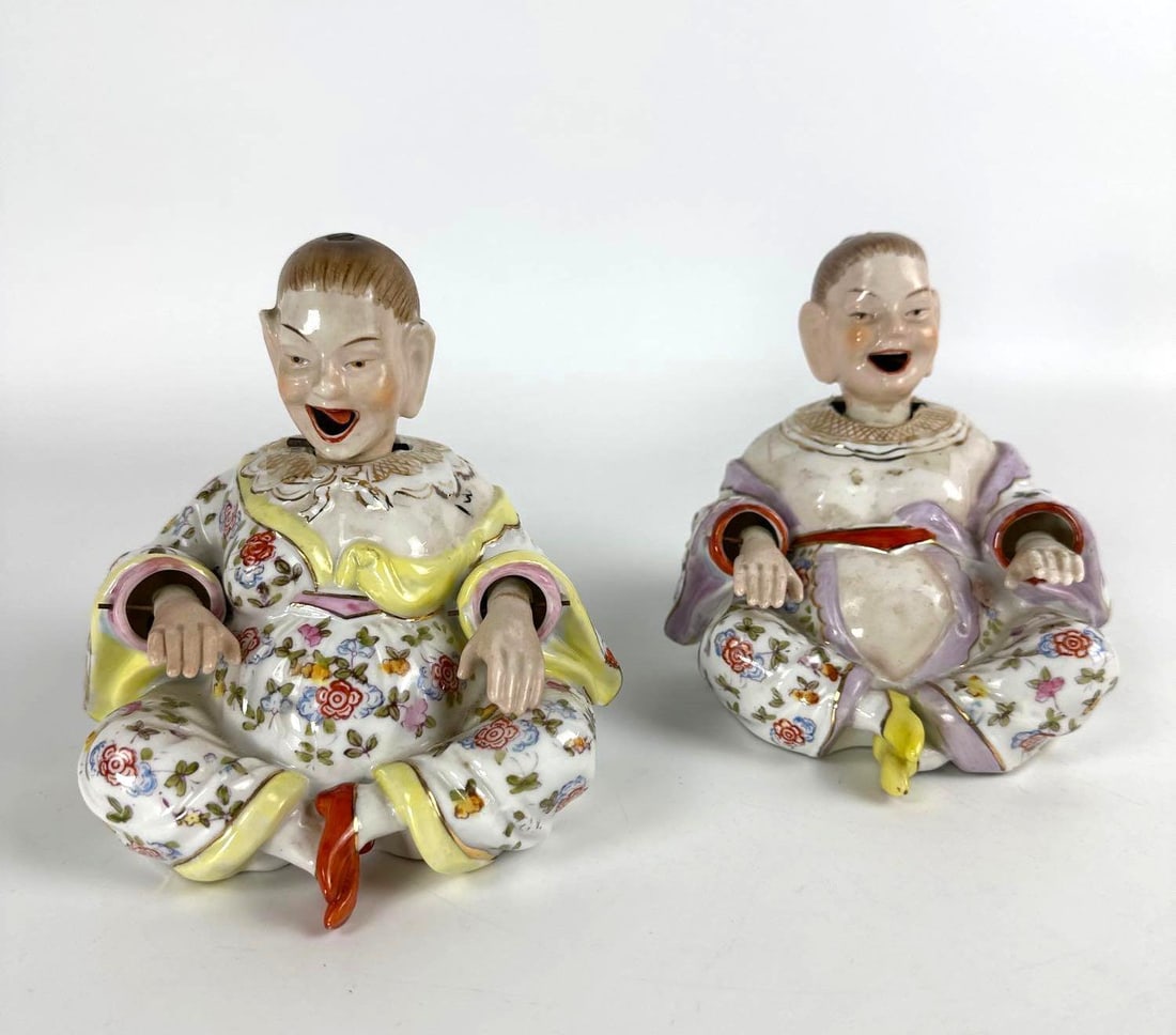 PAIR OF PETITE NODDERS: A pair of petite, seated porcelain nodders, with smiling faces, wearing brightly enameled, floral-patterned robes with their legs crossed. Dimensions: 4.75"H x 6”W x 6”D Maker: Unknown