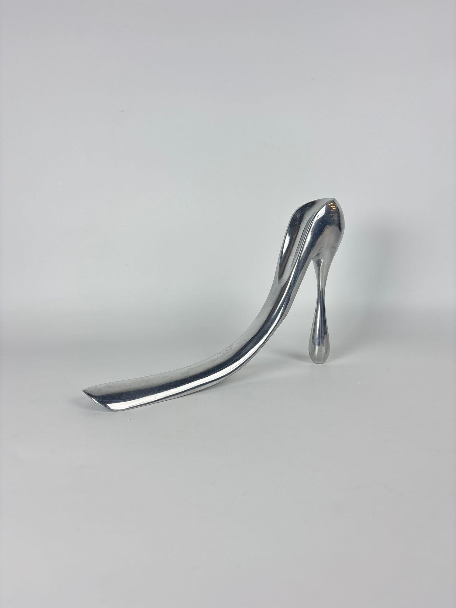 MANOLO BLAHNIK SCULPTURAL ALUMINUM SHOE HORN FOR HABITAT 2004 ANNIVERSARY EDITION: A polished cast aluminum sculpture is a limited-edition shoe horn designed by Manolo Blahnik in the shape of a stiletto heel. Approximate Dimensions: 7.5" x 11.5" x 1.75" Artist or Maker: