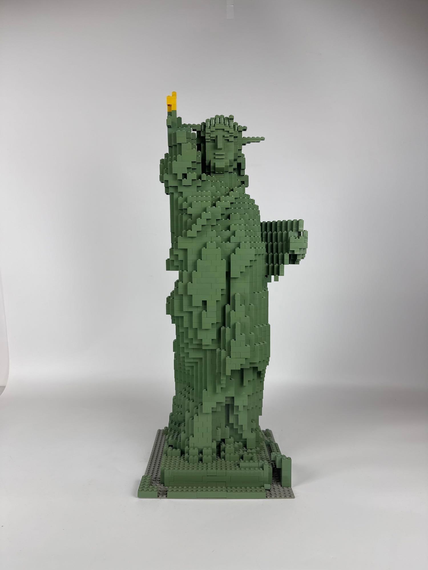 LEGO STATUE OF LIBERTY: This is a large, standing replica of the Statue of Liberty constructed entirely from dark green and yellow Lego bricks. Approximate Dimensions: 27” tall Artist or Maker: Unknown