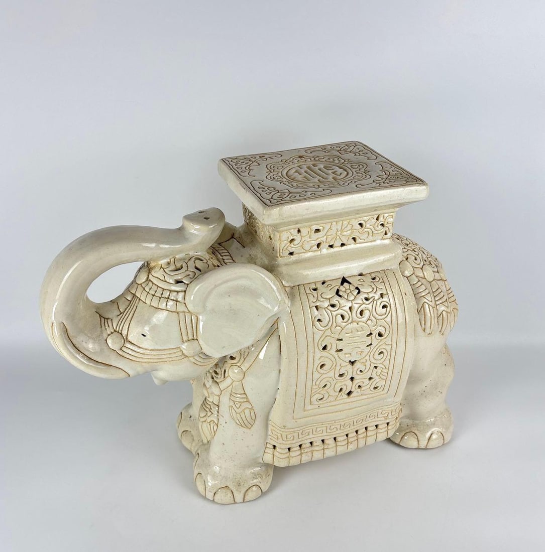 VINTAGE CERAMIC GARDEN ELEPHANT STOOL: Vintage cream-glazed ceramic garden stool in the form of a caparisoned elephant with an ornate pierced saddle, floral relief carvings, and a flat rectangular seat. Approximate Dimensions: 17"H x 21"
