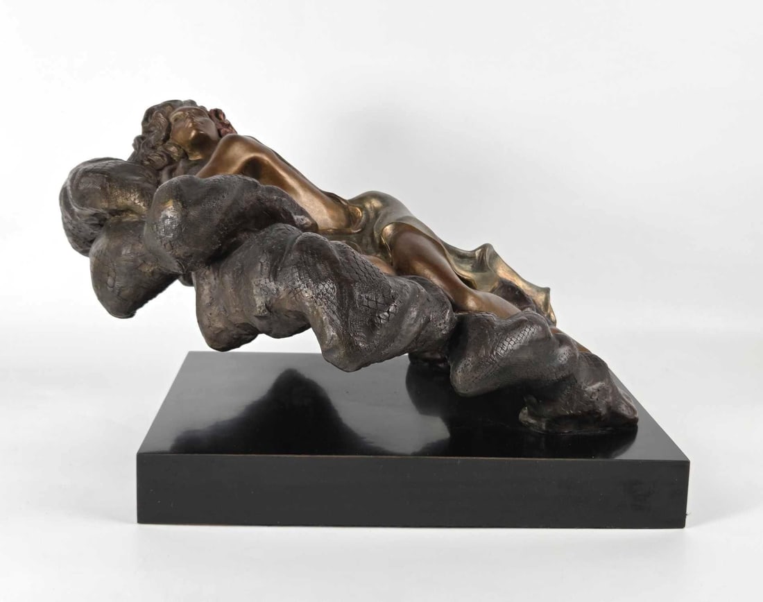 ALICE RIORDAN SIGNED BRONZE SCULPTURE, THE TEMPTRESS: A bronze figural sculpture depicting a woman reclining in voluminous draped fabric on a black base. Approximate Dimensions: 9"H x 17"W x 12"D Artist or Maker: Alice Riordan Provenance:
