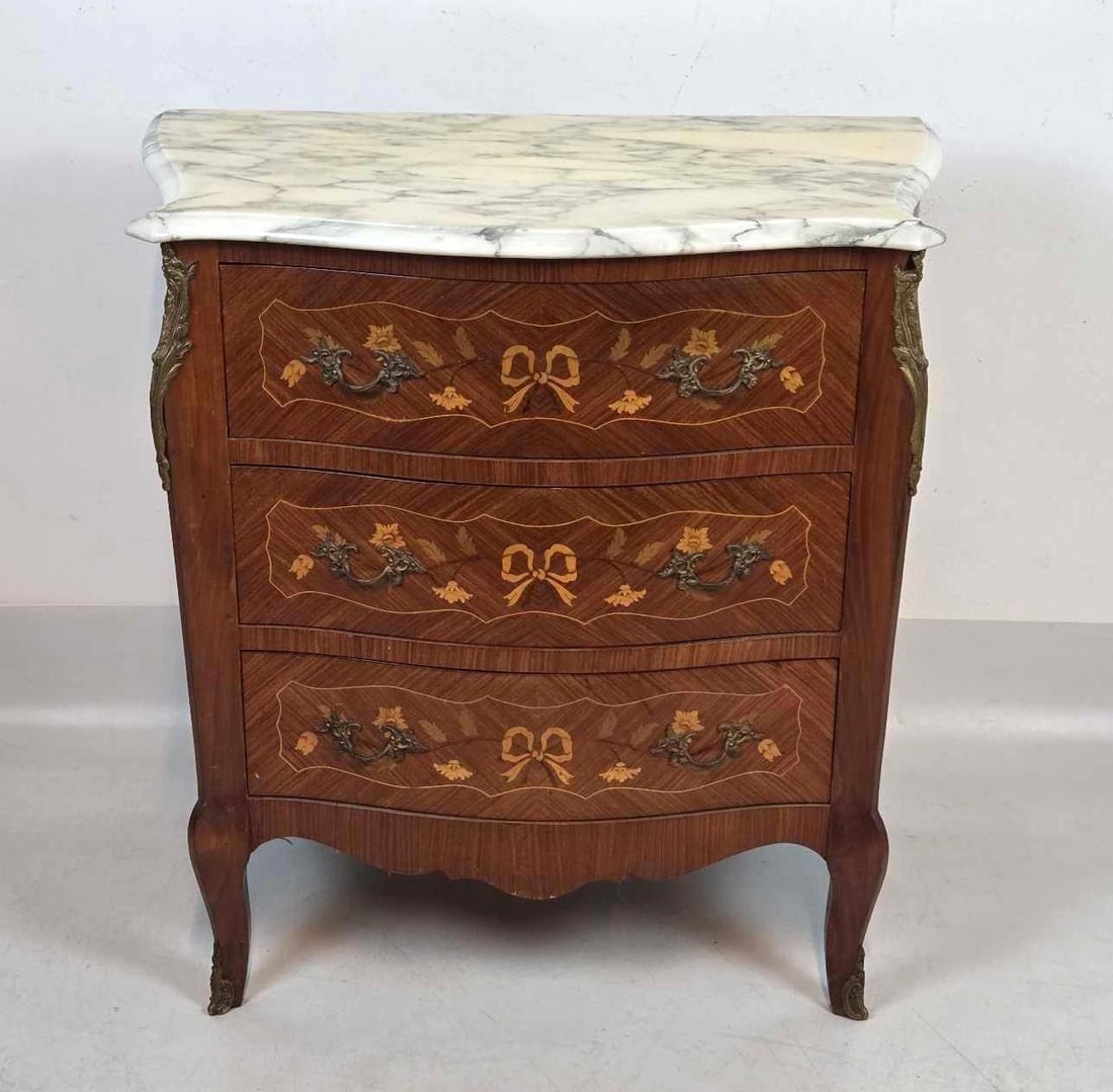 LOUIS XV STYLE MARQUETRY INLAY BRONZE MOUNTED MARBLE TOP COMMODE: A French-style chest of drawers featuring intricate floral and bow marquetry wood inlays, a white Italian marble top, and ornate gilt-bronze ormolu mounts and handles. Approximate Dimensions: 28.25"H