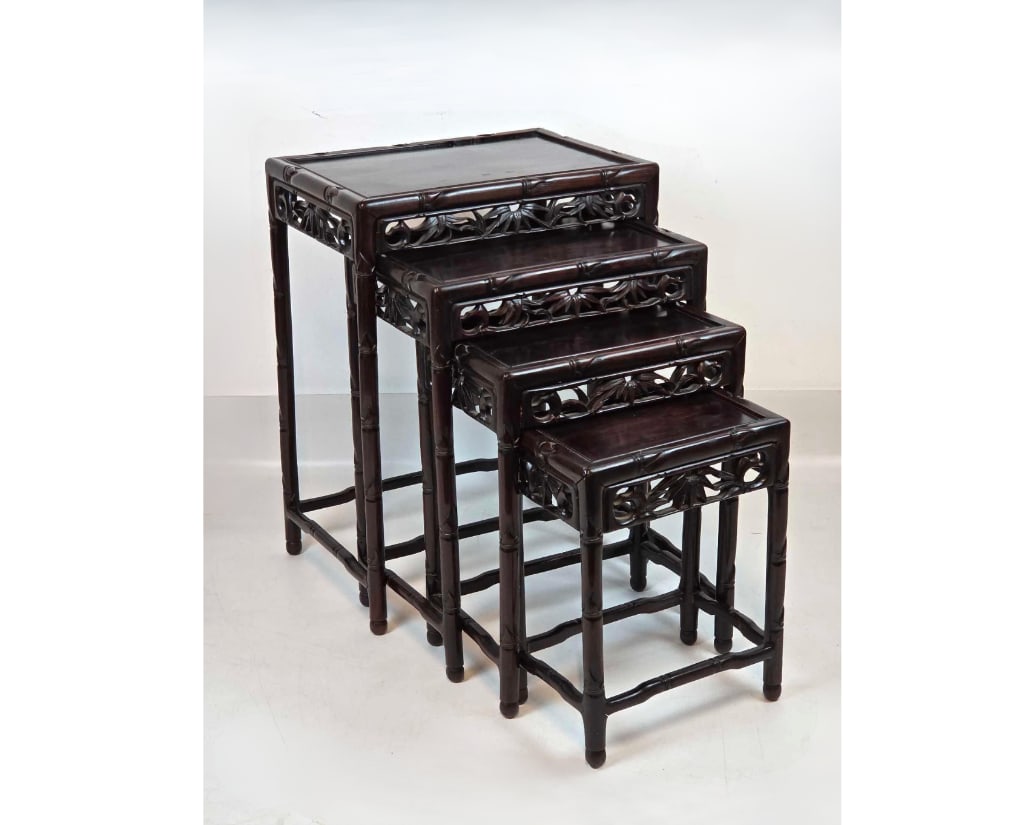 VINTAGE SET OF FOUR CHINESE ROSEWOOD NESTING TABLES WITH BAMBOO MOTIF: Graduated set of four hand-carved dark rosewood tables with faux-bamboo frames and pierced floral aprons. Approximate Dimensions: 26"H X 19"W X 14"D LARGEST 16.5"H X 12.5"W X 8.5"D SMALLEST Artist or