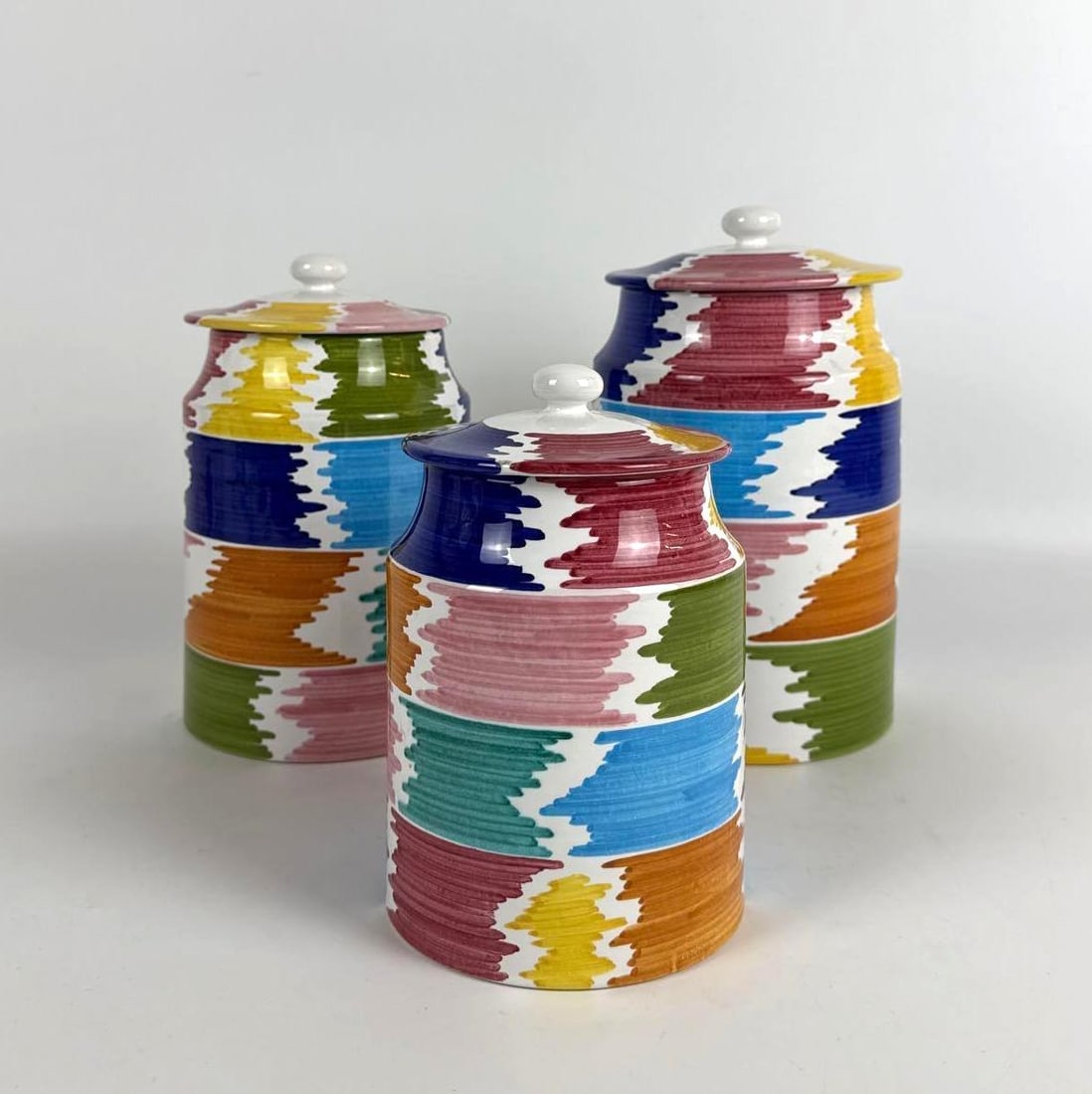 GRAZIA DERUTA ITALY MULTI-COLOR FLAME STITCH PATTERN 3 PC CERAMIC CANISTER SET: *Three ceramic canisters from Grazia Deruta, Italy, are decorated with a colorful, jagged flame stitch pattern. Approximate Dimensions: Largest 10” T x 6” dia Artist or Maker: Gazia Deruta