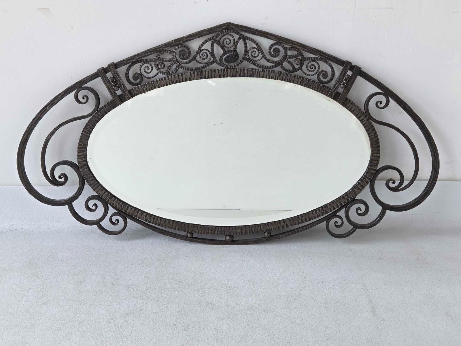 ANTIQUE ART DECO WROUGHT IRON OVAL BEVELLED MIRROR: *This is a large, horizontal oval mirror with a bevelled edge, set into an elaborate, hand-hammered and scrolled wrought iron frame, typical of the French Art Deco period. Approximate Dimensions: 22"