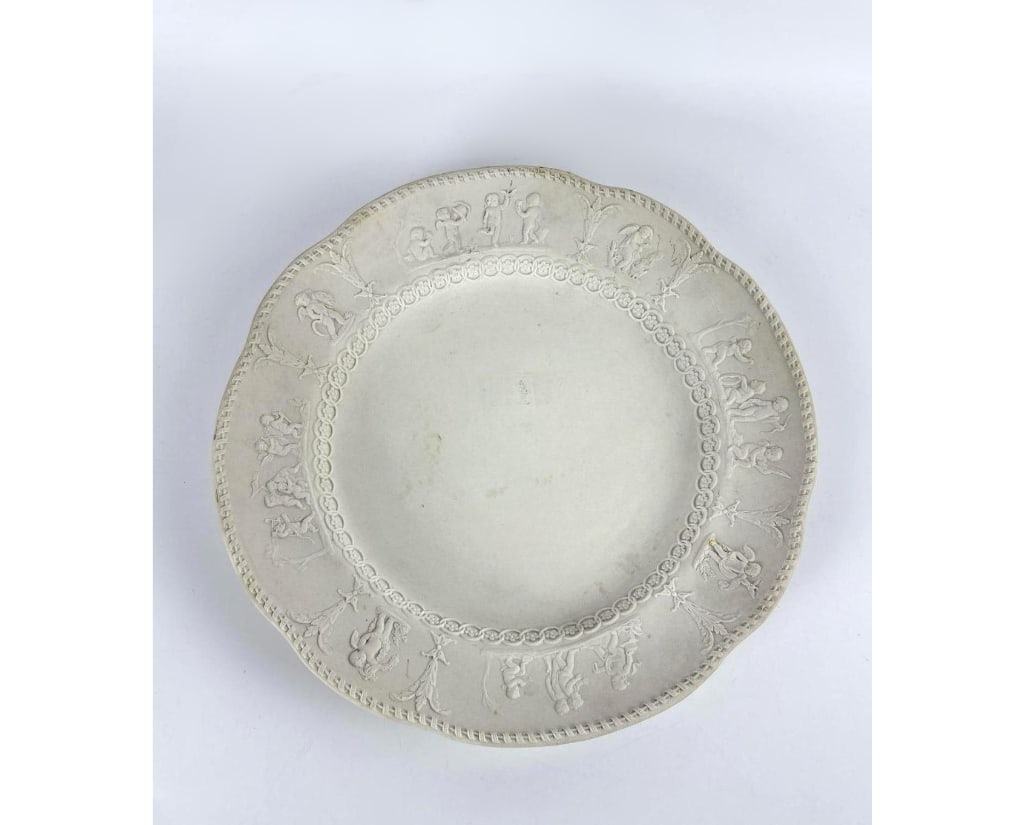 WEDGWOOD JASPERWARE WHITE ON WHITE CHERUB PLATE 11.25": Large matte stoneware charger with neoclassical relief border depicting winged putti and floral garlands. Approximate Dimensions: 11.25" Dia Artist or Maker: Wedgwood Provenance: From a New York Colle