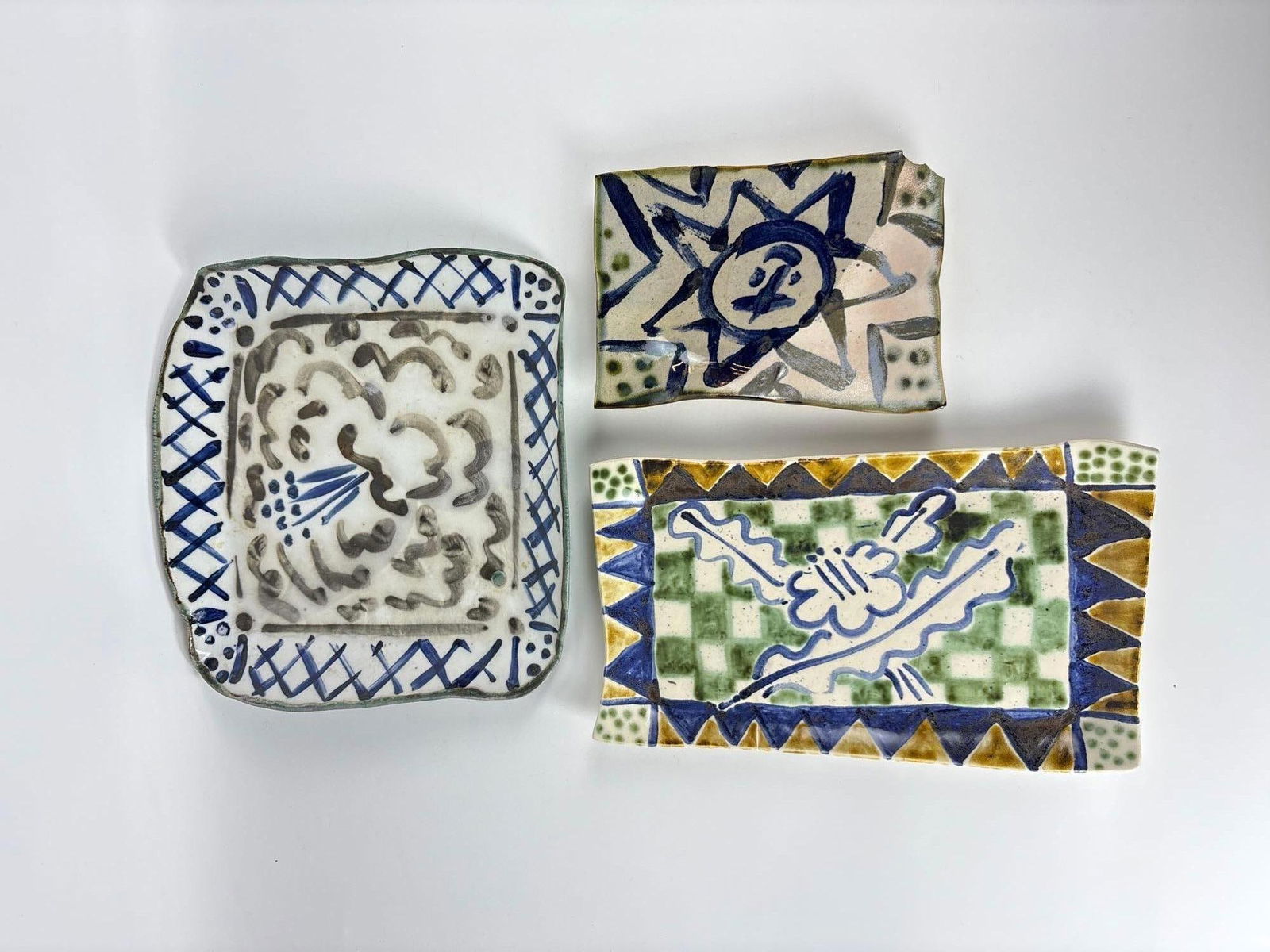 SIGNED HANDMADE CERAMIC TRAYS LOT - STUDIO POTTERY: *This lot is a set of three decorative ceramic plates featuring hand-painted designs including a blue and white checkered pattern and abstract figures. Approximate Dimensions: 11.5" x 10" Arti