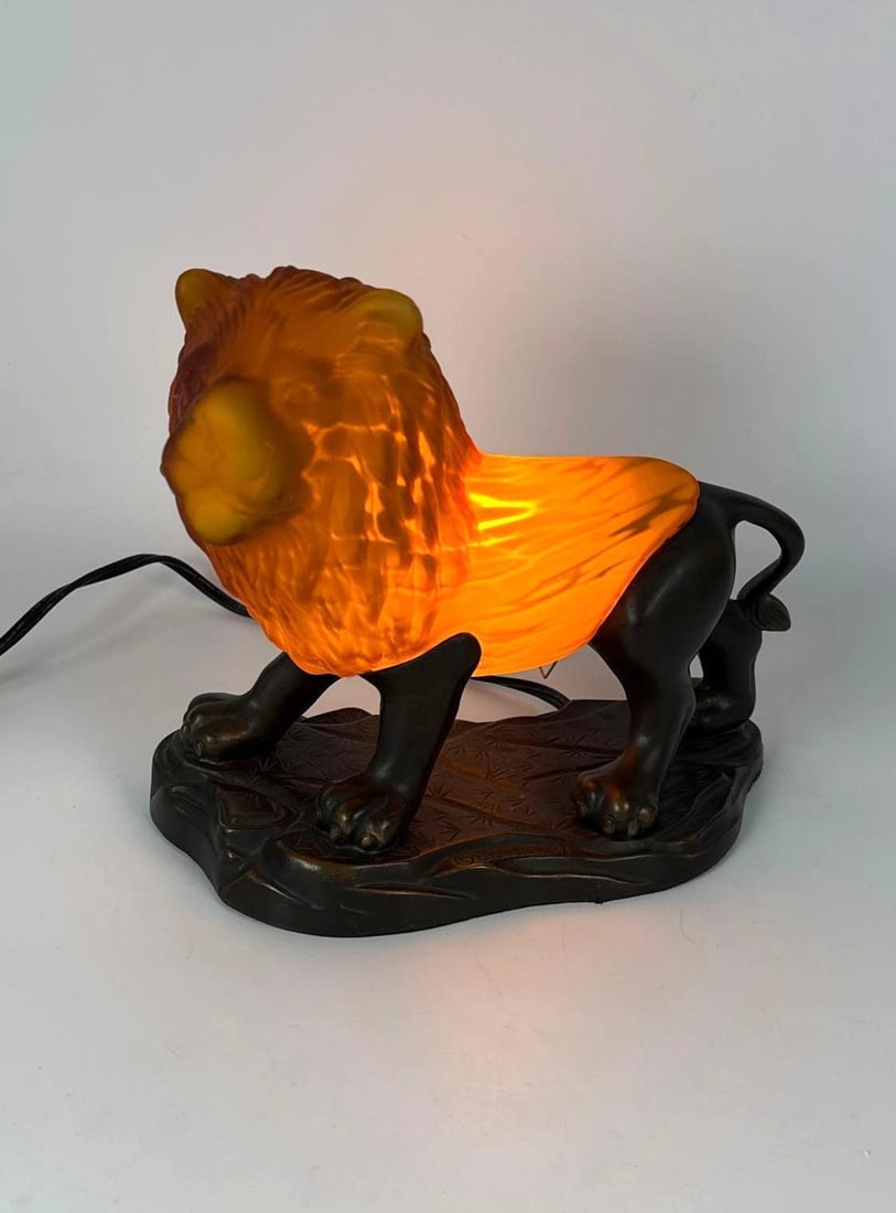 VINTAGE TIN CHI AMBER ART GLASS LION LAMP: Illuminated art glass lion figurine lamp in a warm amber hue mounted on an iron base. Approximate Dimensions: 10”H x 8.5”L x 5”D Maker: Tin Chi Provenance: A New York Collector