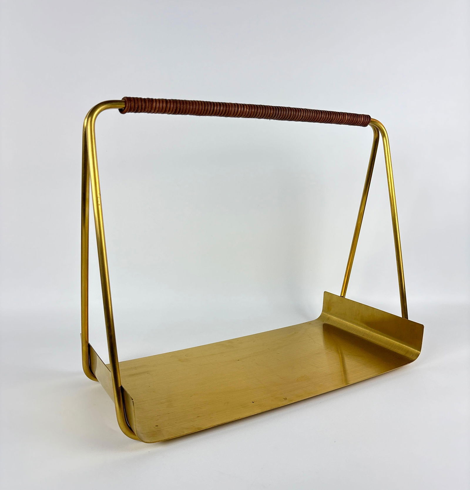 PORT WOOD BASKET WITH WRAPPED HANDLE BY "FERM LIVING": Mid century modern style brass firewood carrier with wrapped handle and open-sided rectangular base by ferm LIVING. Approximate Dimensions: 16"H x 20"W x 9.5"D Artist or Maker: Ferm Living