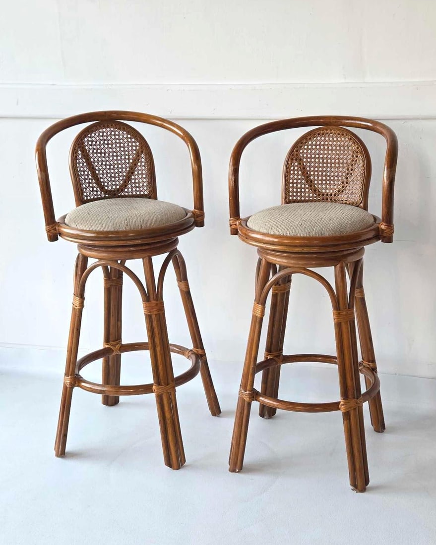 VINTAGE PAIR OF BENT RATTAN CANED BACK SWIVEL BAR STOOLS: A pair of bent rattan bar stools with caned back & upholstered circular seats and wraparound arms. Approximate Dimensions: 41"H x 19"W x 18"D Artist or Maker: Unknown Provenance: From a New York Co