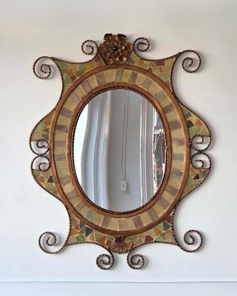 WROUGHT IRON AND MOSAIC MIRROR: A Spanish style, oval mosaic tile mirror with wrought iron spiral details. Approximate Dimensions: 30"L x 23.5"W Artist or Maker: Unknown Provenance: From a New York Collector Notes: Althou