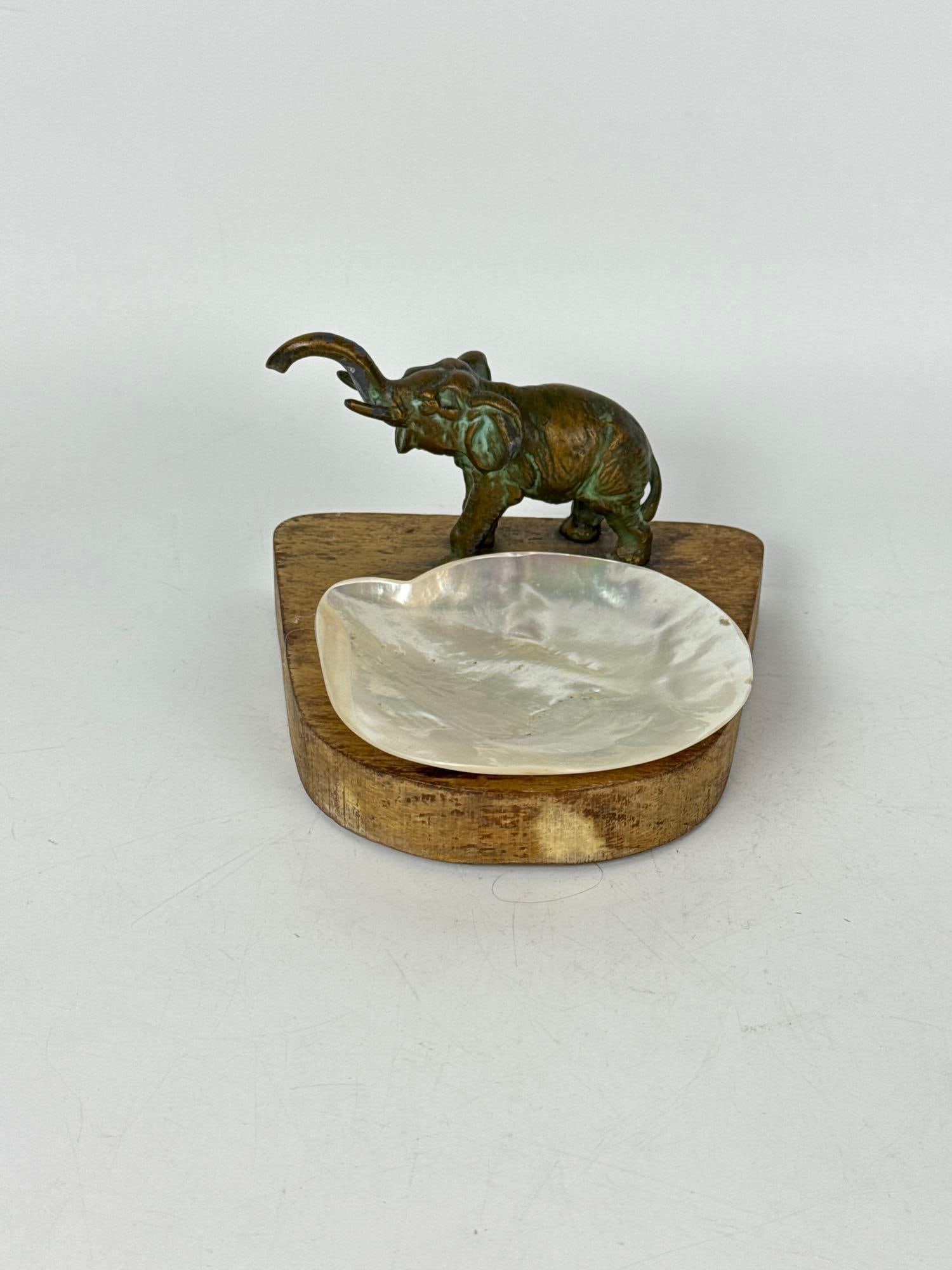 ANTIQUE BRONZE ART DECO ELEPHANT AND MOTHER OF PEARL DISH ON WOODEN BASE: Patinated elephant figure mounted on a carved wood base with an iridescent mother of pearl shell catchall tray. Approximate Dimensions: 3.75” h 5.75 w x 5.5” d Artist or Maker: Unknown Pro