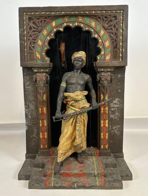 ANTIQUE FRENCH ORIENTALIST COLD-PAINTED SPELTER SCULPTURE OF A GUARD: Polychrome metal figure of a Nubian warrior holding a sword within an architectural Moorish archway flanked by elephant head capitals. Approximate Dimensions: 38.5"h x 24"w x 12"d Artist or Maker: Un