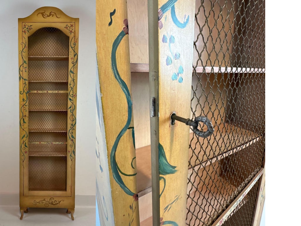 VINTAGE ITALIAN STYLE HAND-PAINTED NARROW CABINET BOOKCASE: *Slim-profile yellow ochre wooden display cabinet with hand-painted floral vine motifs, wire mesh door, and original skeleton key. Approximate Dimensions: 82.5”H x 22.25”W x 7”D Ar
