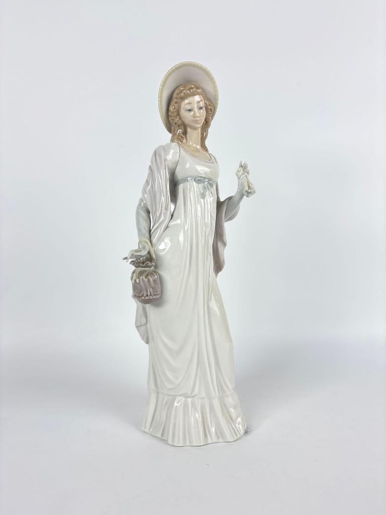 LLADRO SPAIN "DAINTY LADY" PORCELAIN FIGURINE: *A glazed porcelain sculpture of a woman in a broad brimmed hat holding a handkerchief and handbag, issued in 1974 and retired in 1985. Approximate Dimensions: 13.75" h x 5.5" Artist or Make