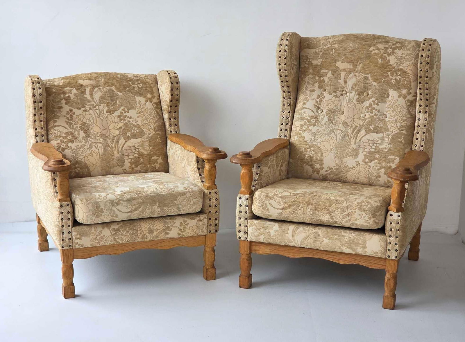 PAIR OF HENNING KJAERNULF OAK EASY CHAIRS, C. 1970'S: A pair of Danish mid-century carved oak "his & hers" style wing back and lounge chairs with floral upholstery and brass nail head trim. Larger Approximate Dimensions: 41"H x 31"W