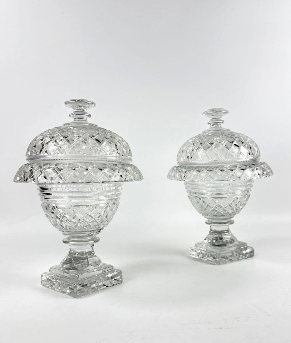 PAIR OF CUT GLASS LIDDED COMPOTE BOWLS: Duo of elegant clear lead crystal pedestal vessels featuring diamond geometric facets and matching domed covers Approximate Dimensions: 10.5”h x 8”dia Artist or Maker: Unknown Provenance: