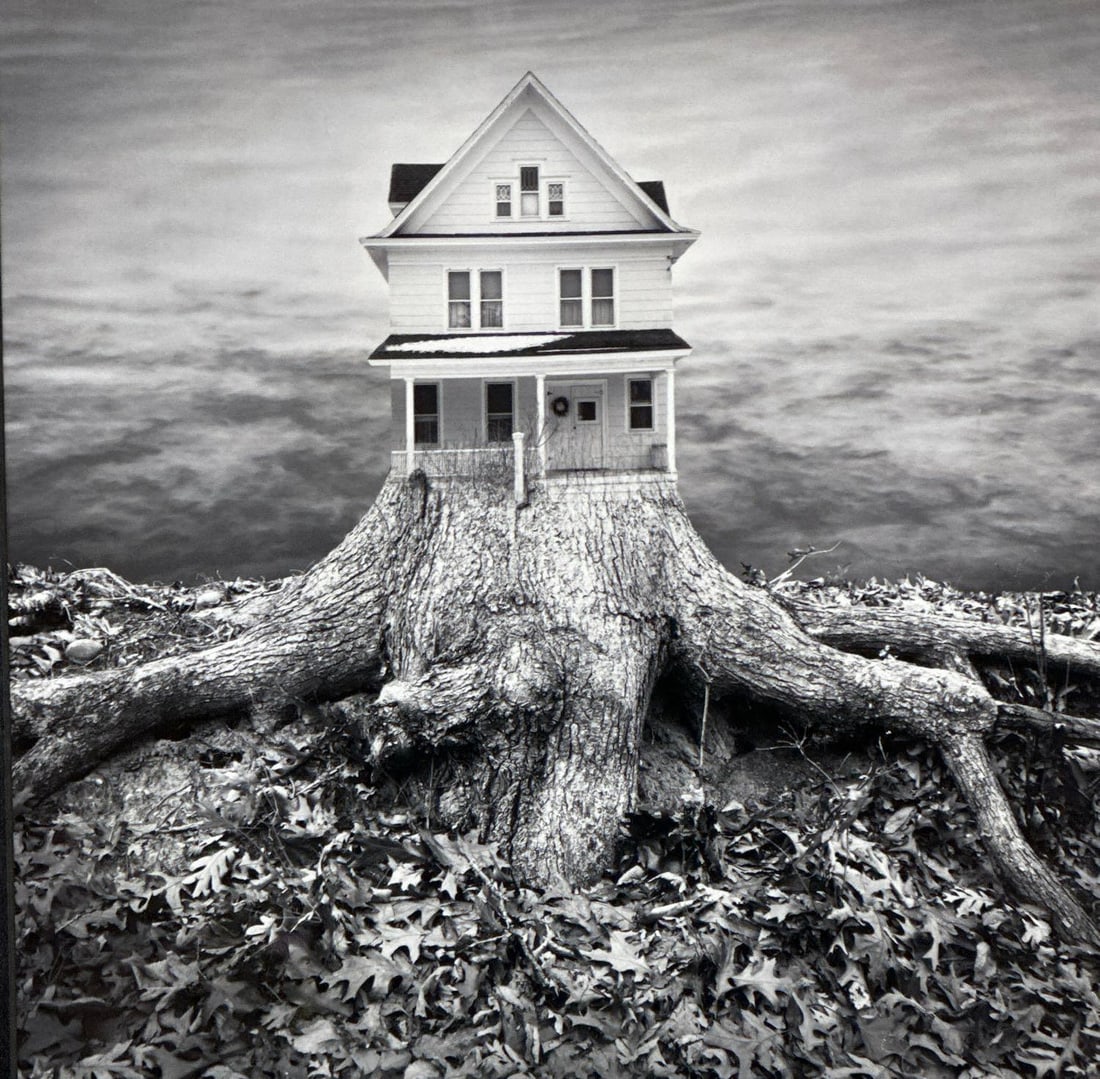 SURREALIST BLACK AND WHITE PHOTOGRAPHY IN THE STYLE OF JERRY UELSMANN: Composite grayscale image of a house merging into a large tree stump root system Approximate Dimensions: 11”x11” Framed 17.5”x17.5” Artist or Maker: Unknown