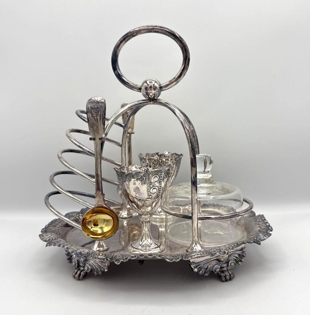 EDWARDIAN SILVER PLATED BREAKFAST CRUET WITH SILVER SPOONS: Antique English silver-plated breakfast service stand with integrated five-slot toast rack, two pedestal egg cups, glass preserve jar, and included silver spoons weighing 1.1 oz t. Approximate Dimens