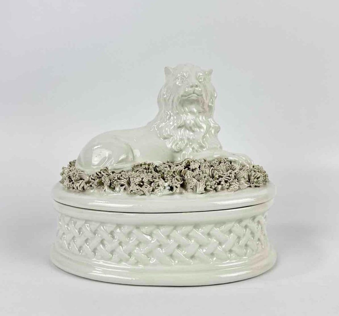 EARLY 20TH CENTURY ITALIAN STAFFORDSHIRE STYLE CERAMIC LION BOX: White glazed pottery recumbent lion figure atop a floral encrusted lid with a relief-molded trellis weave basket base. Approximate Dimensions: 5.75”h x 7”w x 5”d Artist or Maker: Unk
